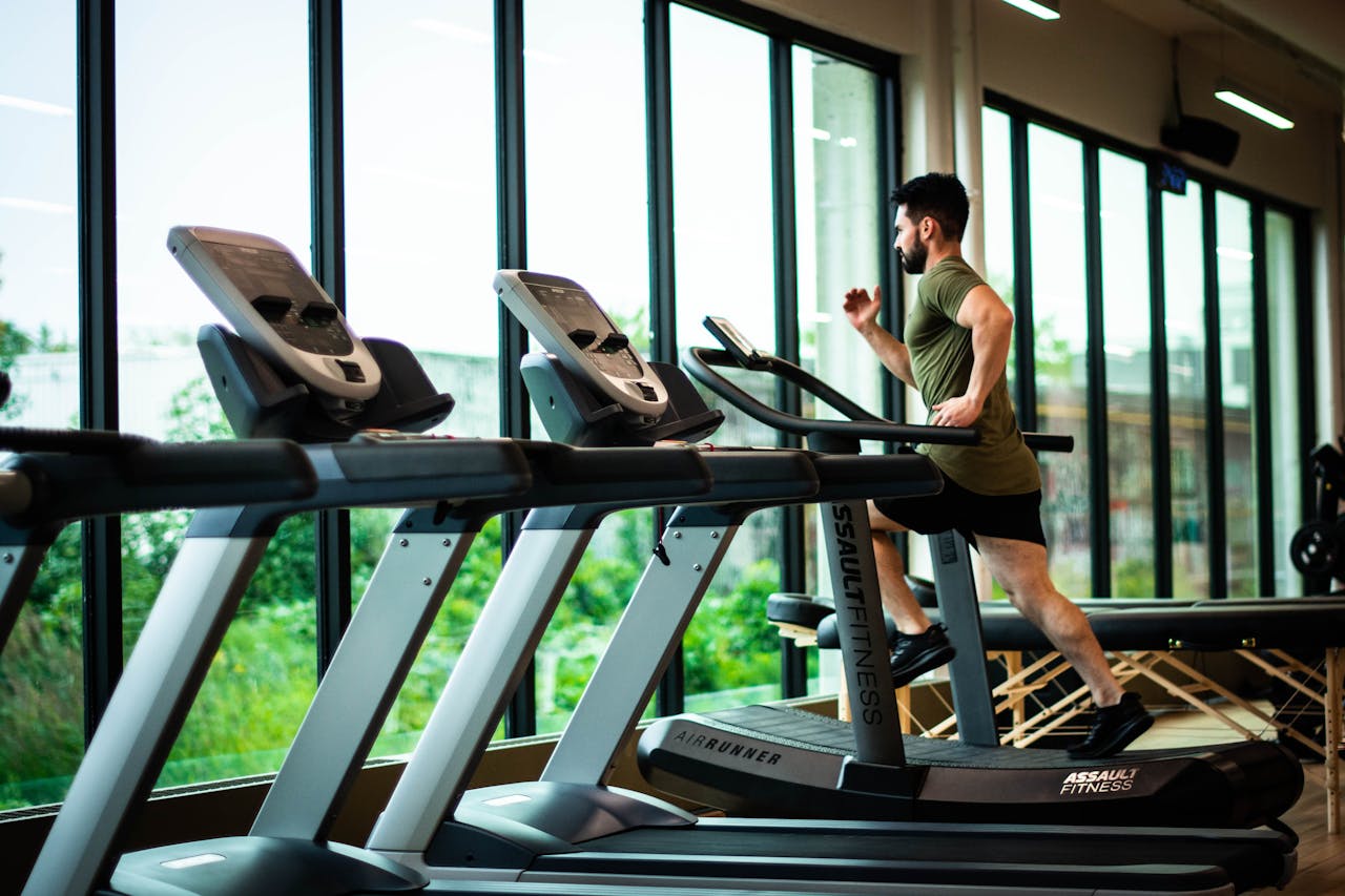 Home Young man workouts on treadmill in modern gym with large windows and natural light.